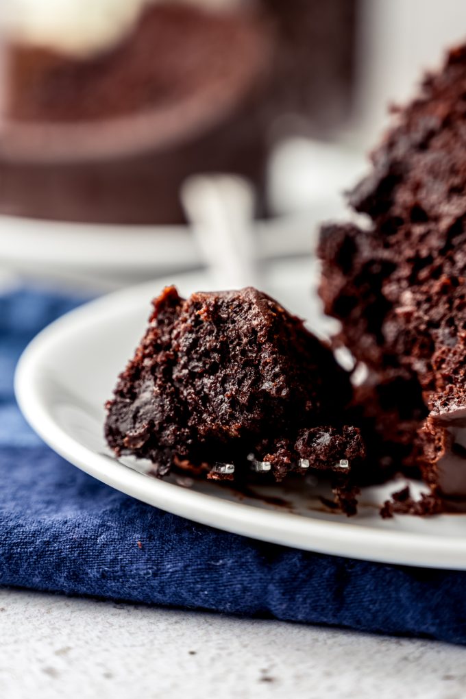 A closeup of a fork with a bite of chocolate Bundt cake on it sitting next to the slice of cake on a plate.