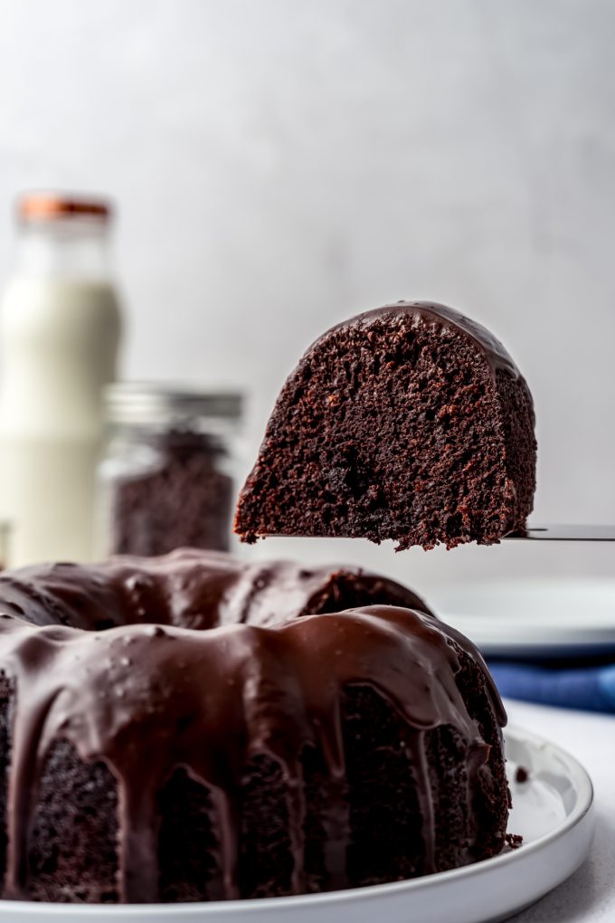 Someone is removing a slice of chocolate Bundt cake from a sliced cake on a plate.