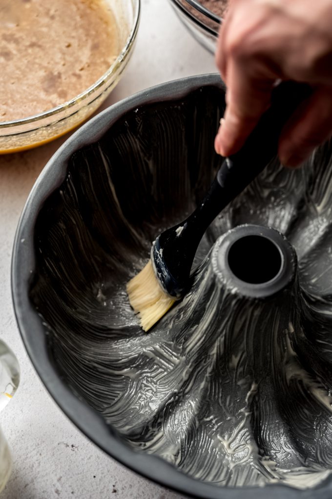 Someone is brushing a Bundt pan with cake release using a pastry brush.
