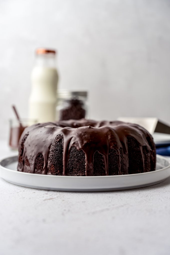 A chocolate Bundt cake on a plate with a glass bottle of milk in the background.