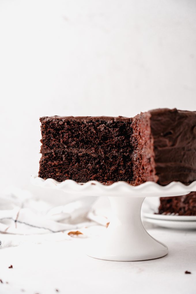 A chocolate layer cake on a cake stand and it has been sliced so you can see the cross section.