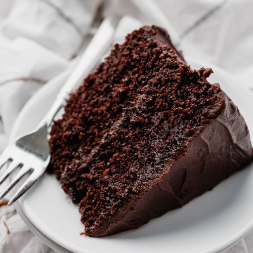 A slice of chocolate layer cake on a plate with a fork.