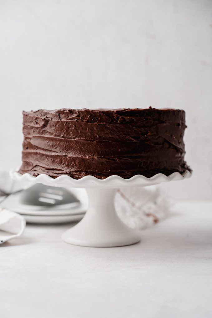 A chocolate cake on a white fluted cake stand.