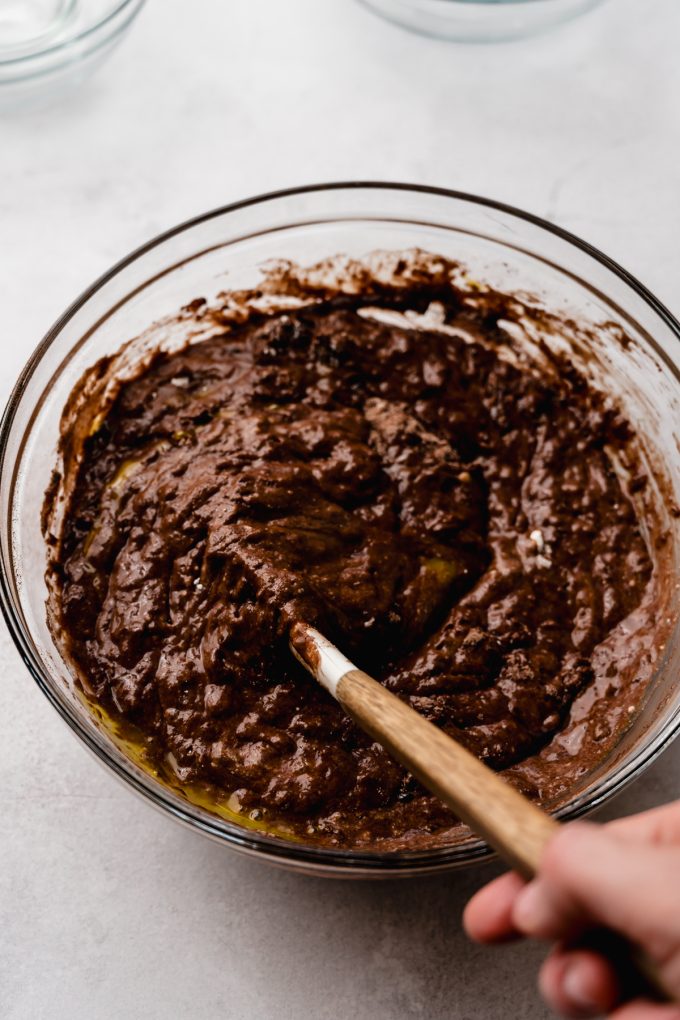 Someone is stirring chocolate cake batter with a spatula.