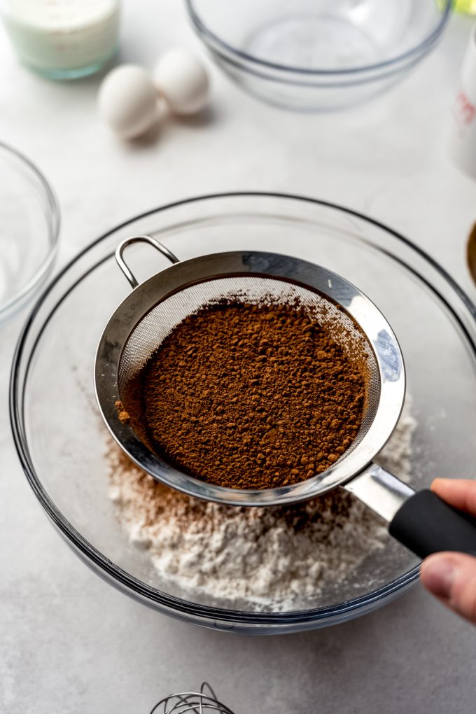Someone is sifting cocoa powder into dry ingredients.