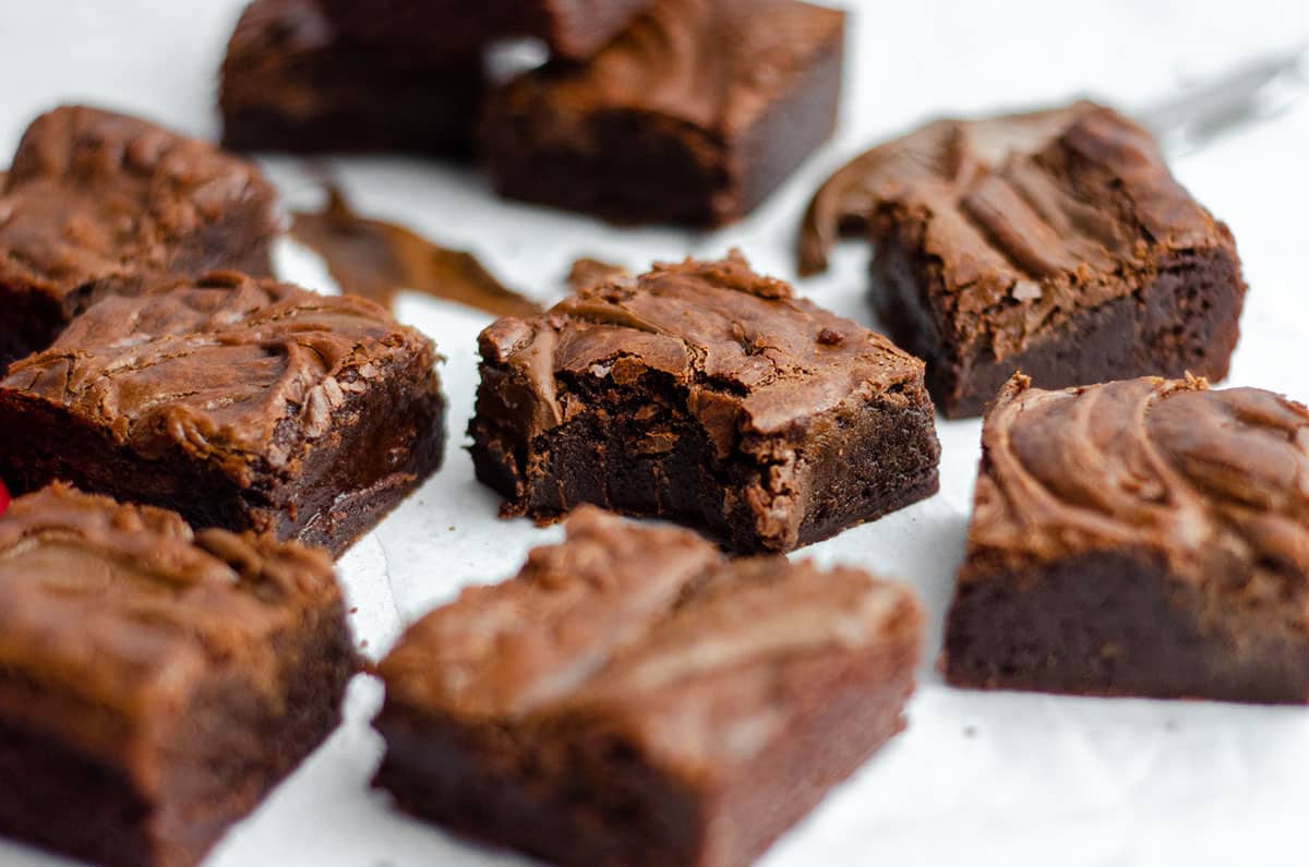 fudgy nutella brownies on a white surface and one with a bite taken out of it