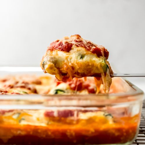 Someone is lifting a portion of zucchini ravioli from a casserole dish.
