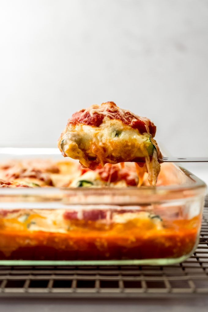 Someone is lifting a portion of zucchini ravioli from a casserole dish.