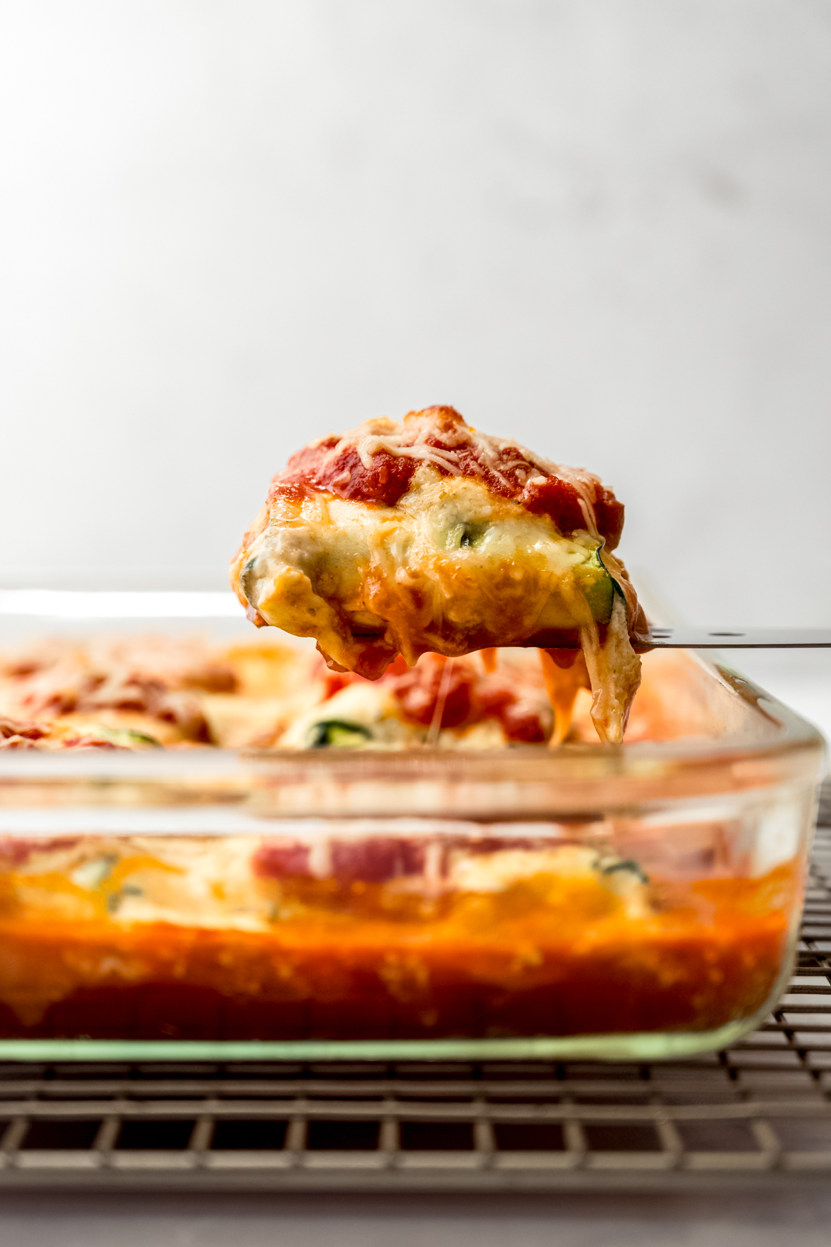 Someone is lifting a portion of zucchini ravioli from a casserole dish.