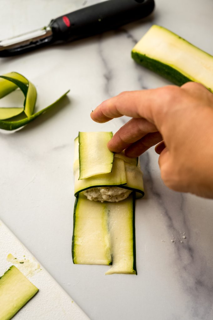 Someone's hand folding zucchini ravioli into a pocket.