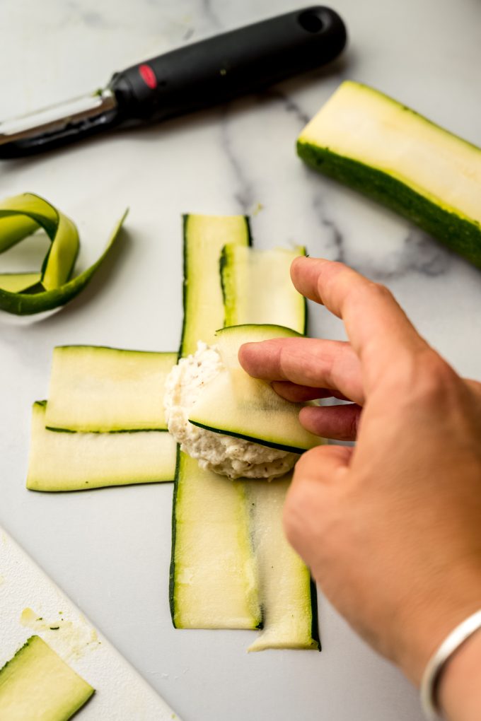 Someone's hand folding zucchini ravioli into a pocket.