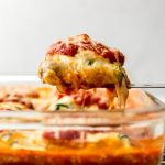 Someone is lifting a portion of zucchini ravioli from a casserole dish.