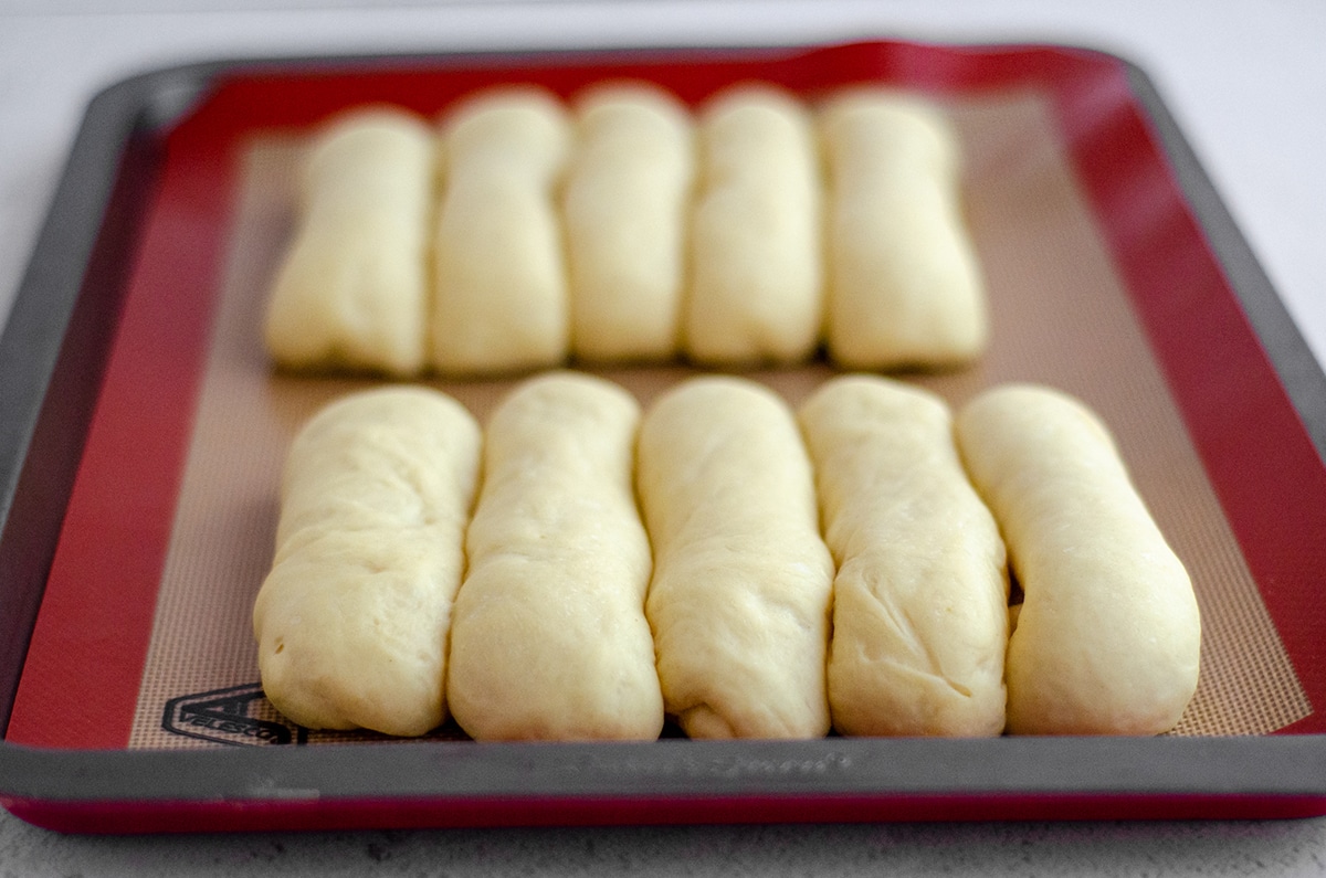 shaped hot dog buns on a baking sheet after they have risen