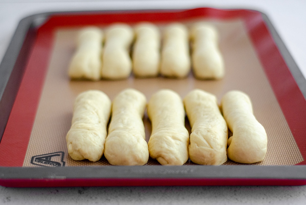 shaped hot dog buns on a baking sheet ready to rise