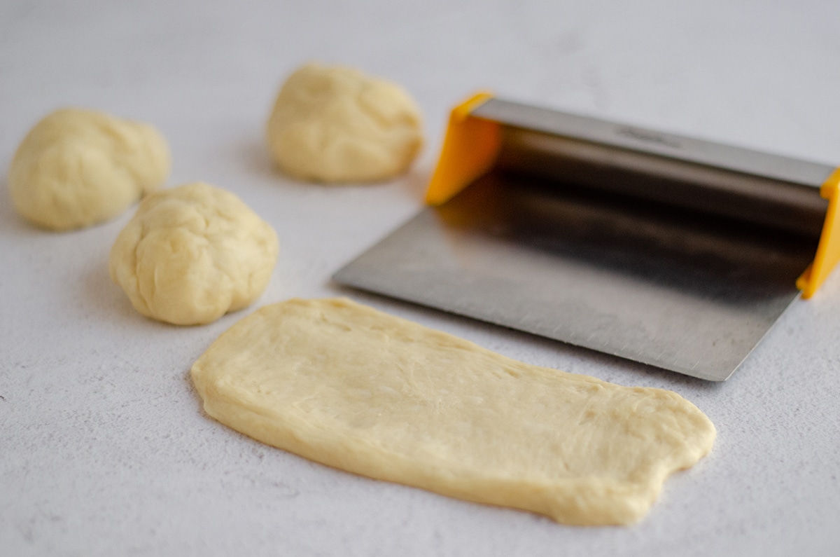homemade hot dog bun dough split into pieces and being measured for accuracy before shaping