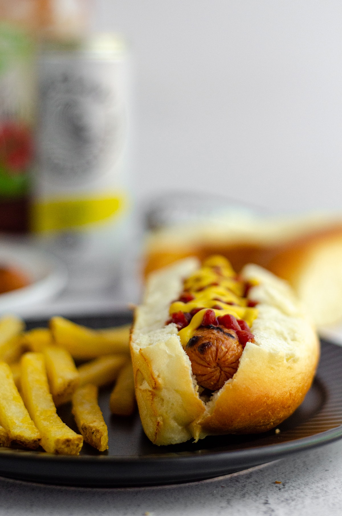 hot dog in a homemade hot dog bun with a squirts of ketchup and mustard sitting on a black plate with french fries