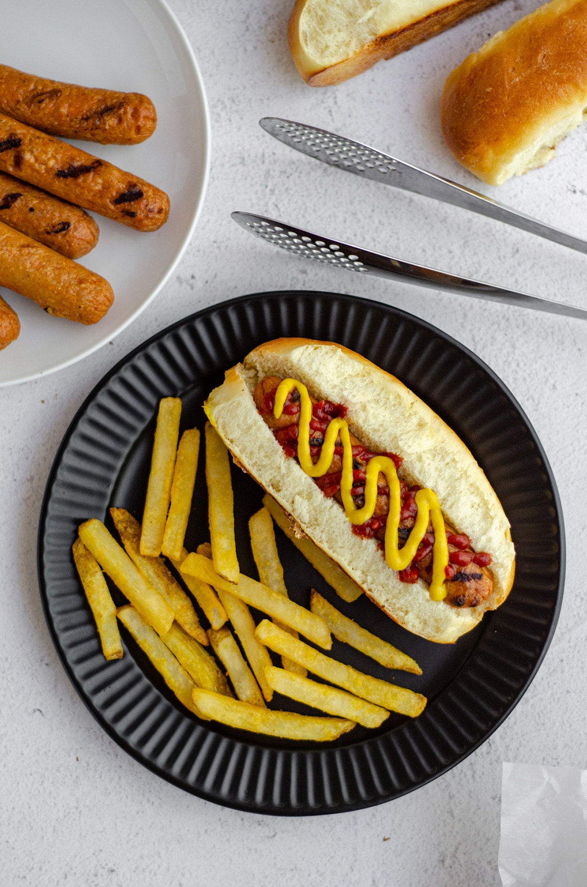 aerial photo of hot dog in a homemade hot dog bun with a squirts of ketchup and mustard sitting on a black plate with french fries