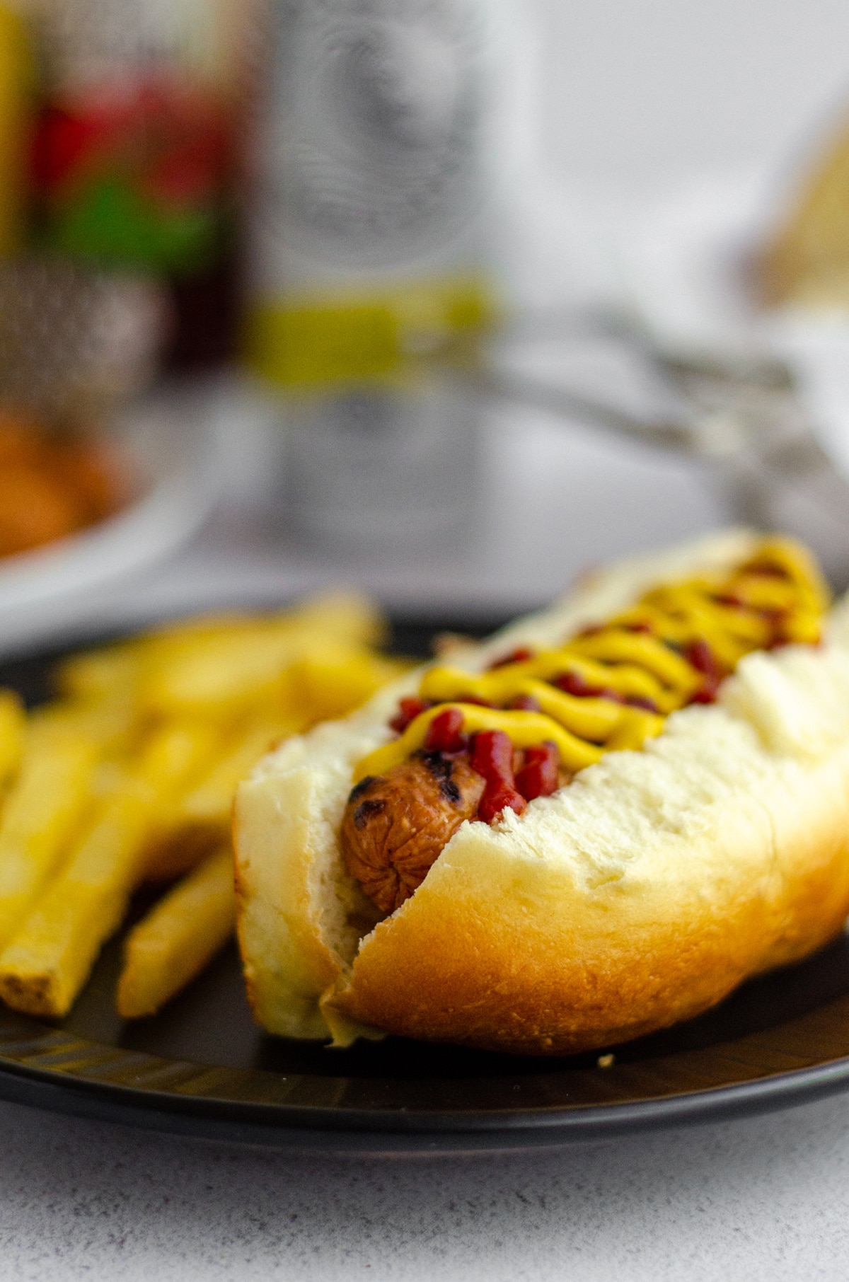 hot dog in a homemade hot dog bun with a squirts of ketchup and mustard sitting on a black plate with french fries