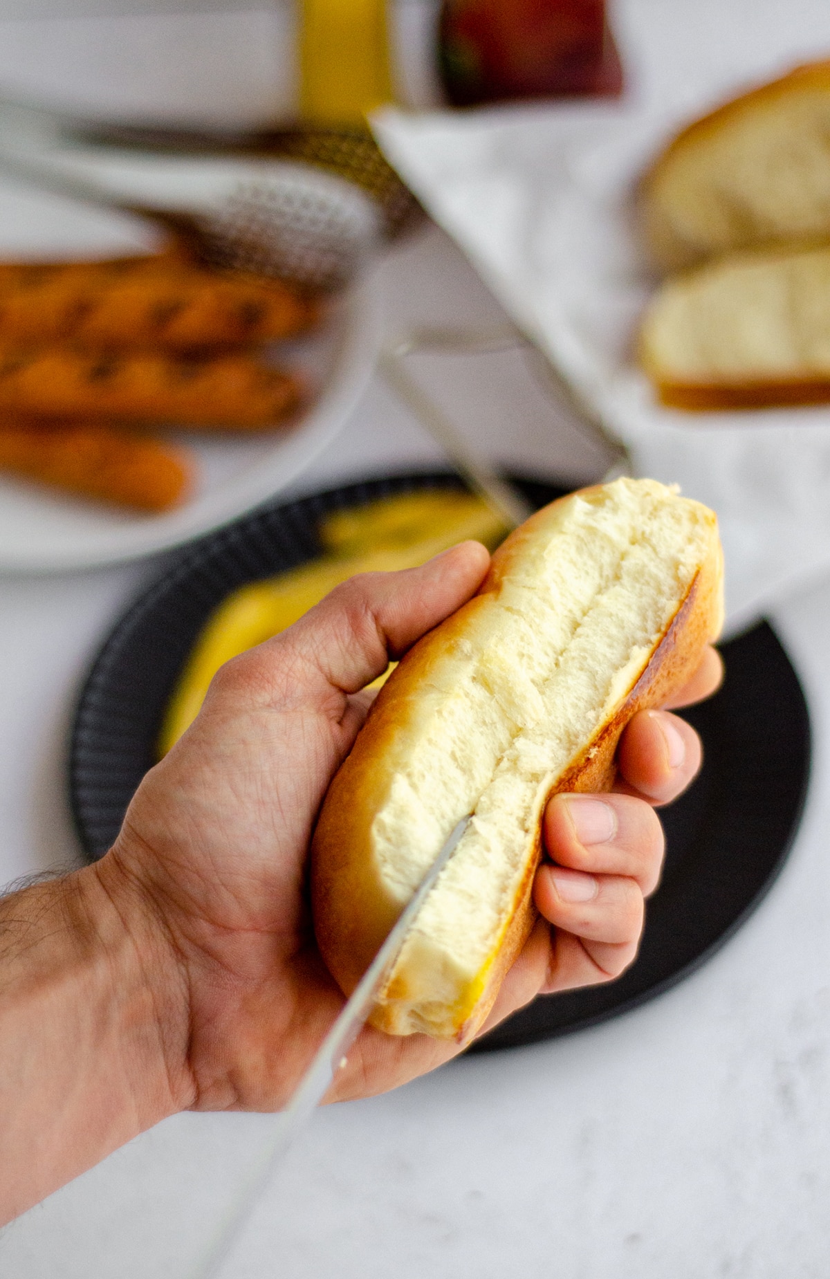 a hand holding a homemade hot dog bun and cutting it open with a knife