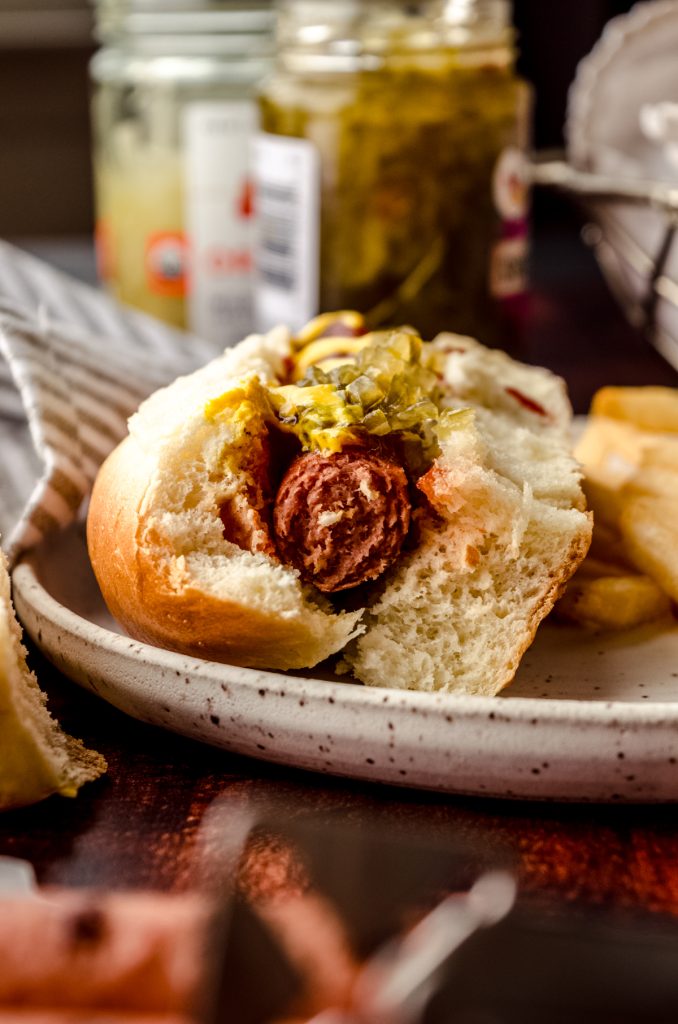 A hot dog in a homemade hot dog bun sitting on a plate with a bite taken out of it.