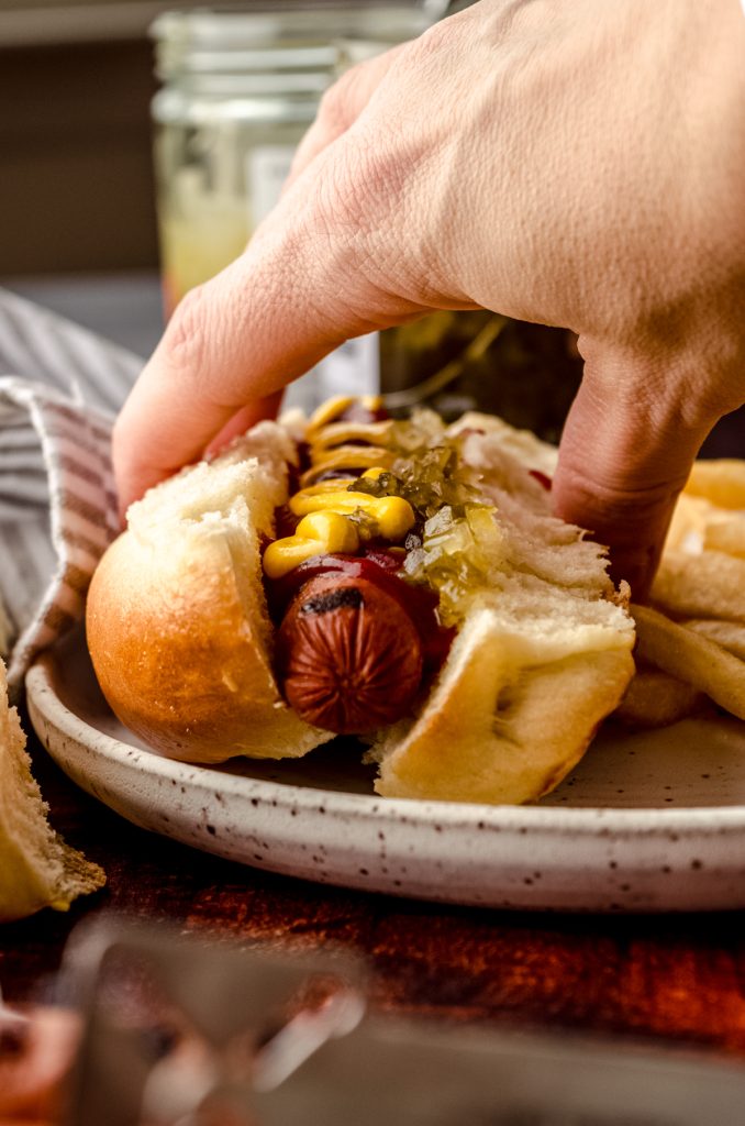 Someone is grabbing a hot dog in a homemade hot dog bun off of a plate.