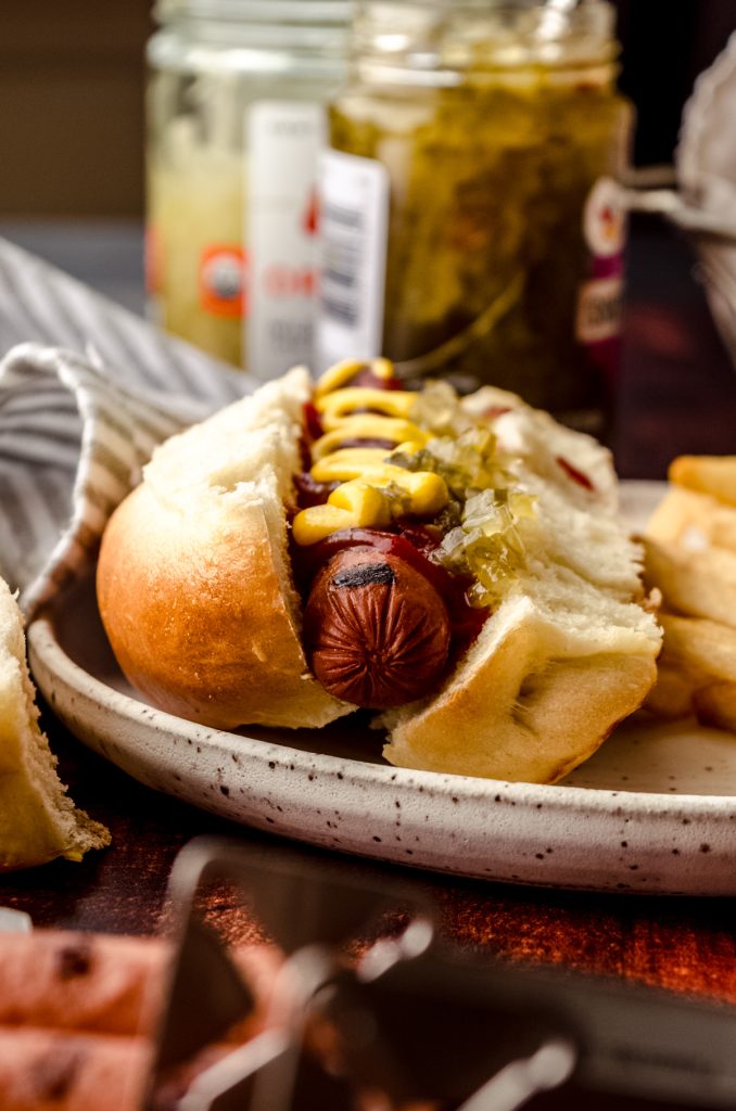 A hot dog in a homemade hot dog bun off of a plate.