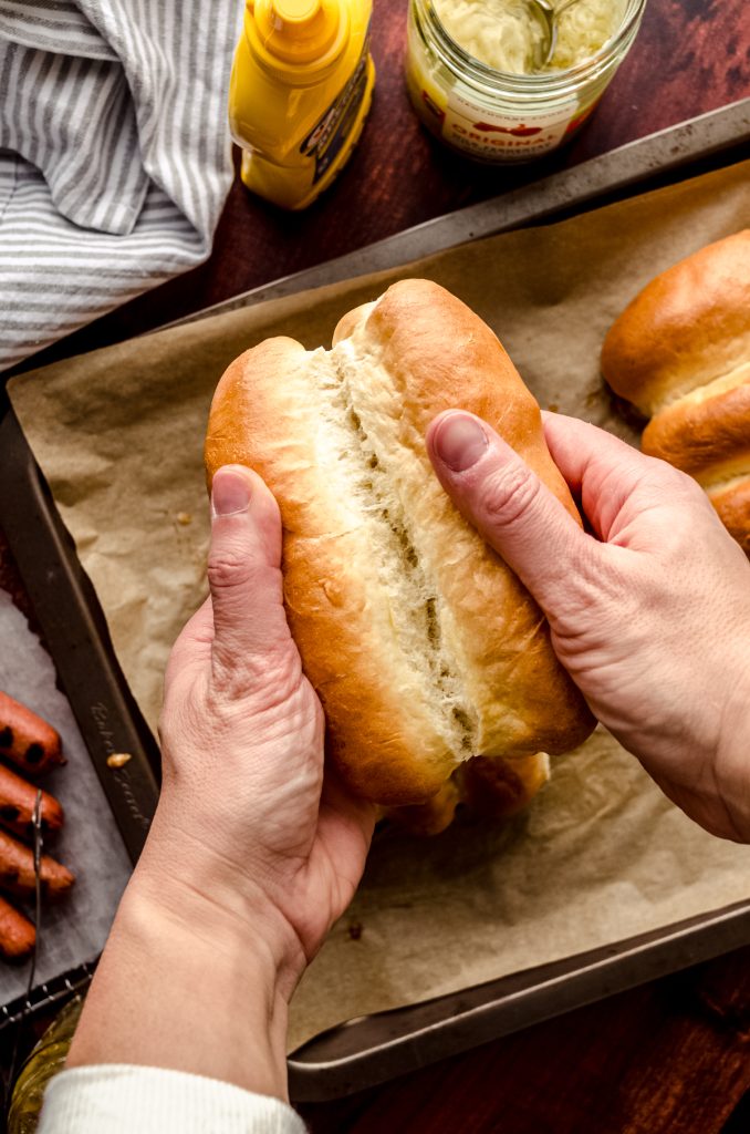Someone is pulling homemade hot dog buns apart with their hands.