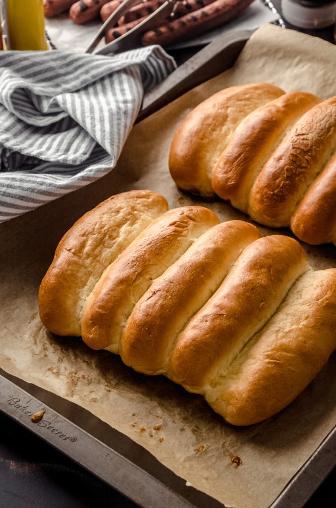 Homemade hot dog buns on a baking sheet.