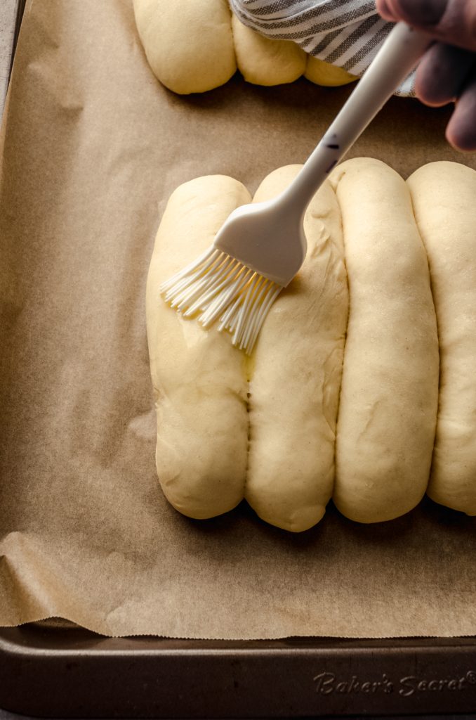 Someone is brushing an egg wash onto shaped homemade hot dog buns.