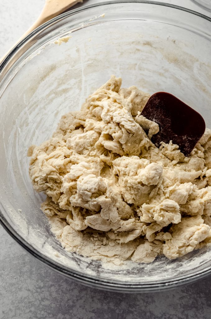 Homemade hot dog bun dough in a bowl with a bench scraper.