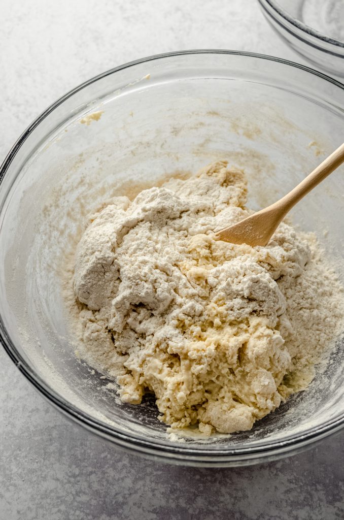 Homemade hot dog bun dough coming together in a bowl with a wooden spoon.