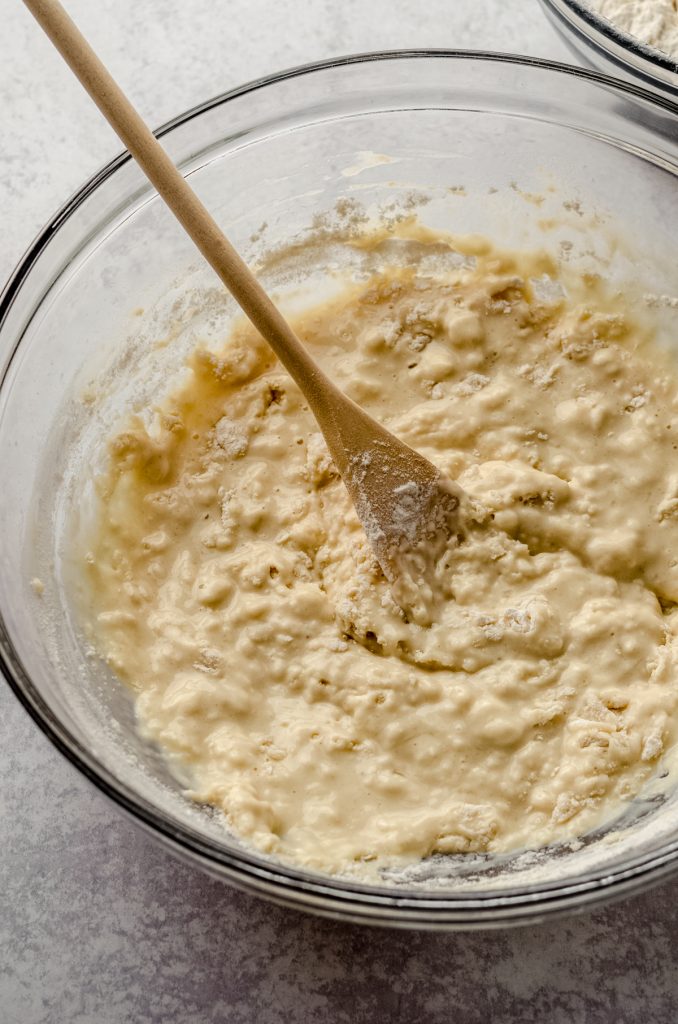 Homemade hot dog bun dough coming together in a bowl with a wooden spoon.