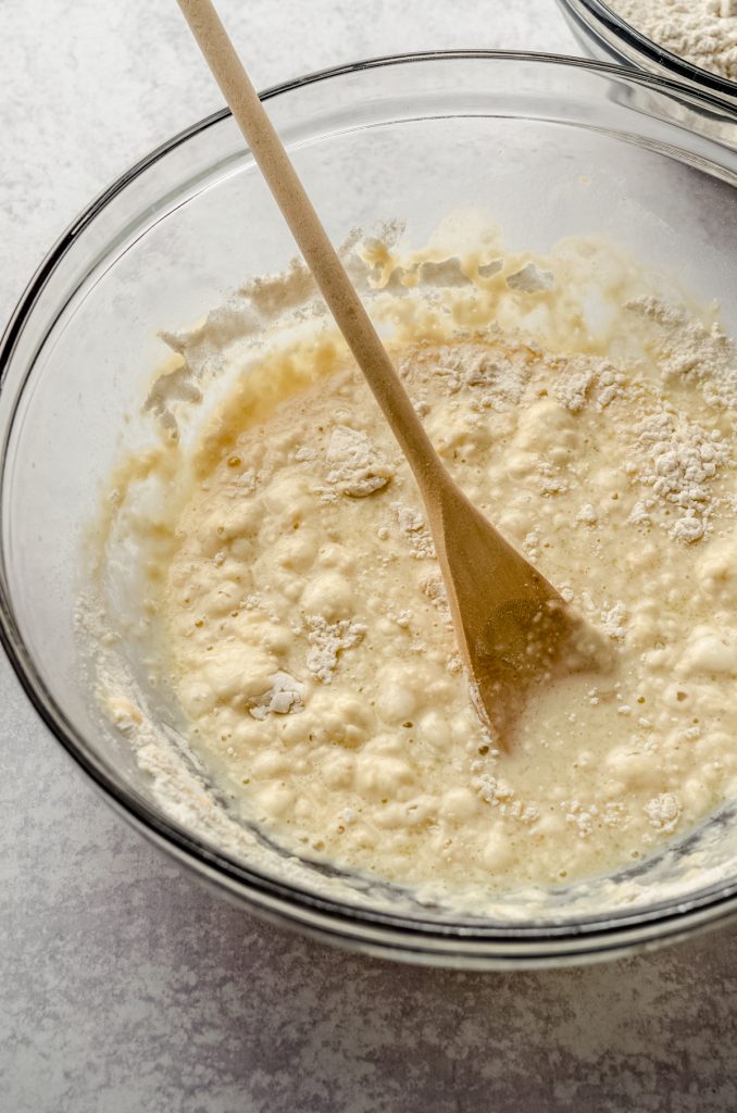 Homemade hot dog bun dough coming together in a bowl with a wooden spoon.