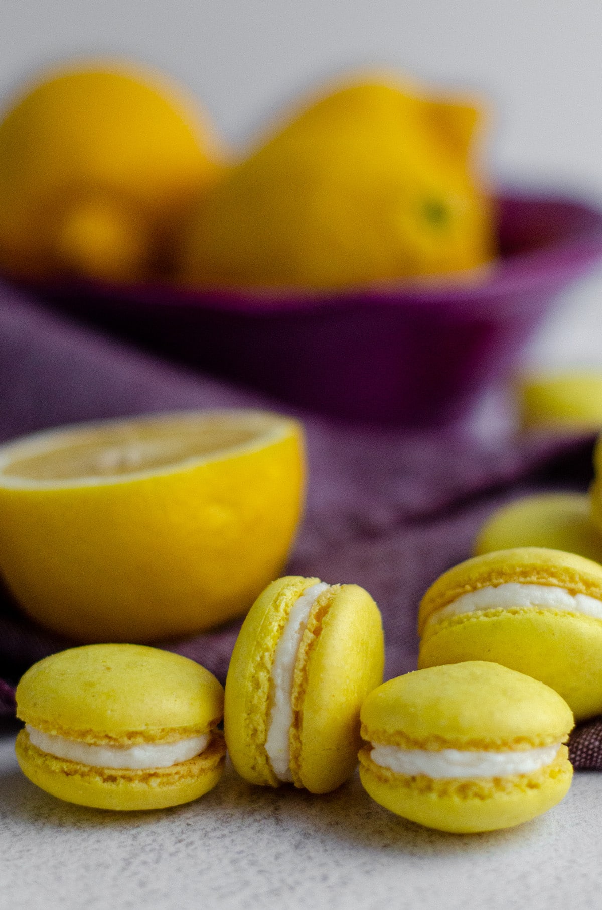 lemon macarons with a purple kitchen towel and sliced lemons in the background