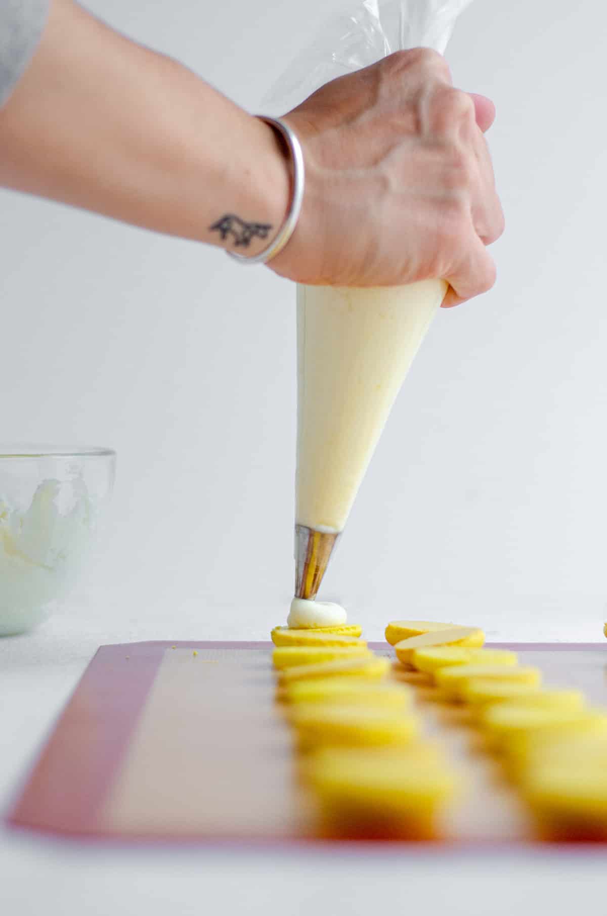 hand piping lemon buttercream onto macaron halves 