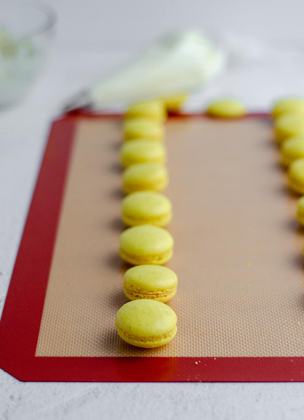 lemon macarons on a baking sheet getting ready to assemble with frosting on the inside