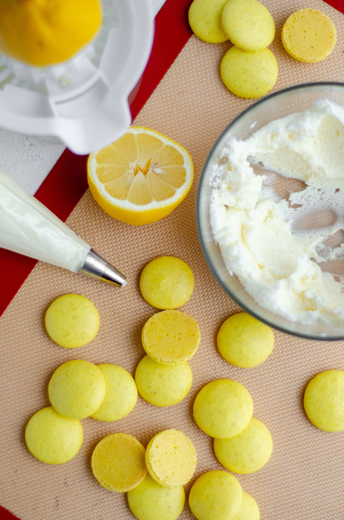 aerial photo of lemon macarons and a bowl of frosting with a piping bag full of frosting ready to be assembled 