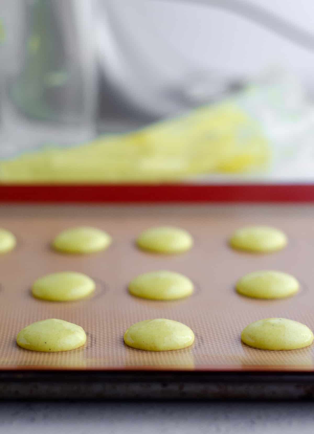lemon macarons piped onto a baking sheet ready to bake