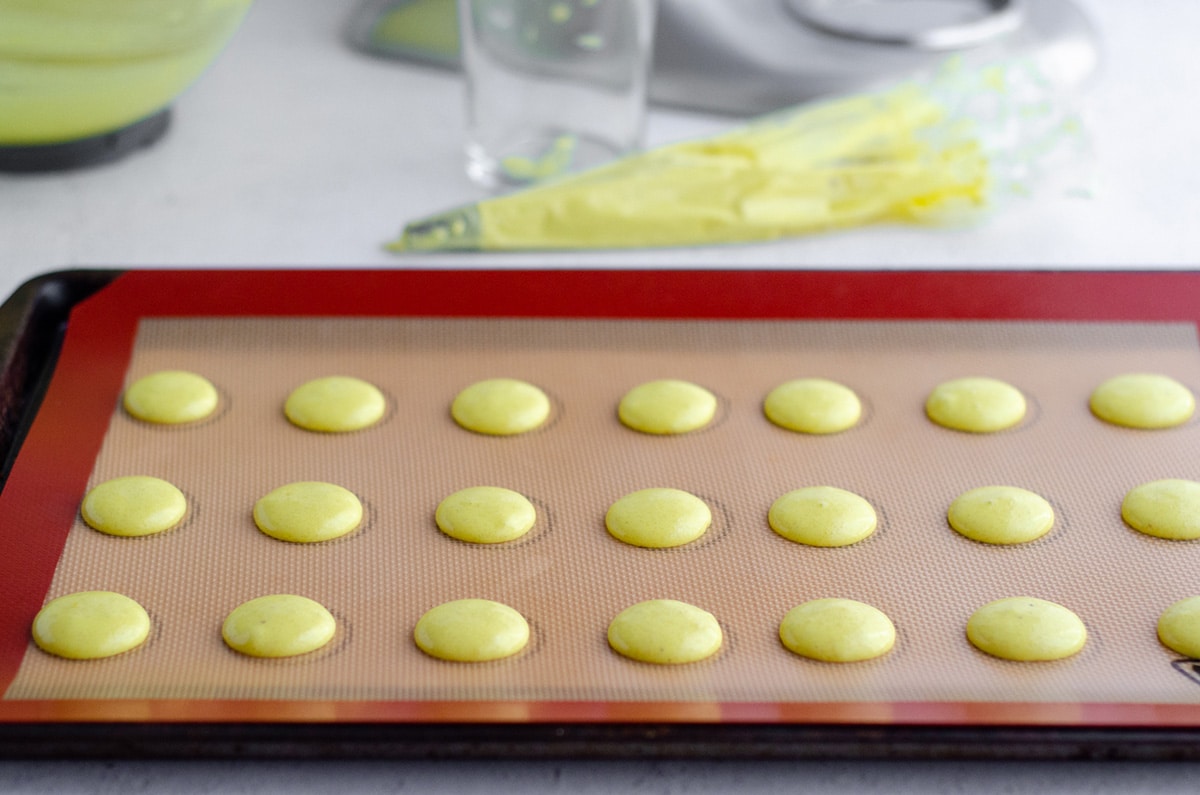 lemon macarons piped onto a baking sheet ready to bake