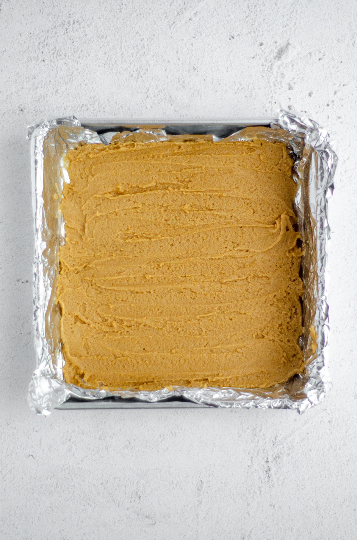 aerial photo of the peanut butter cookie base of brownies in a foil lined pan