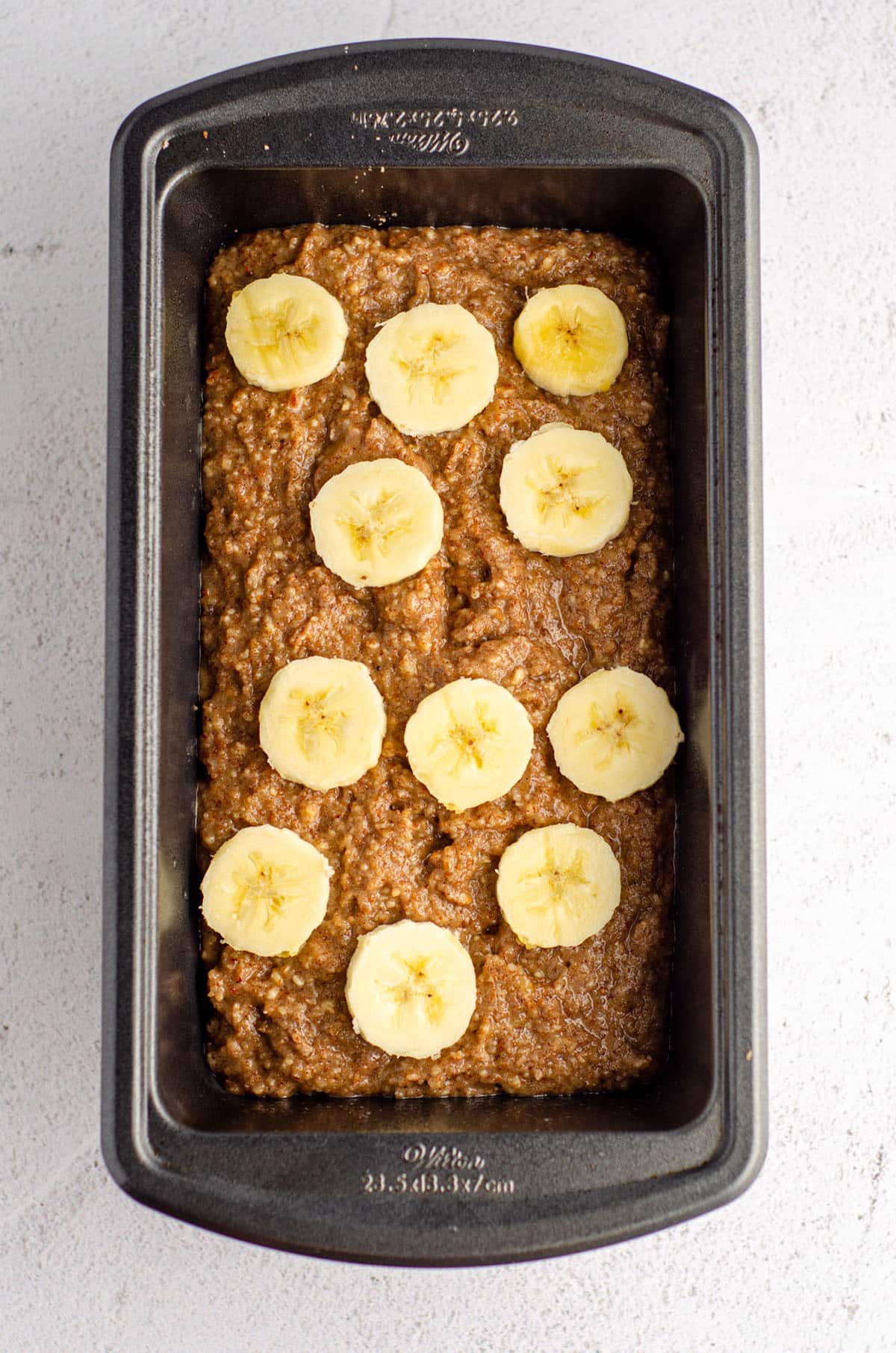 almond flour banana bread batter in a loaf pan with sliced bananas on top of the batter