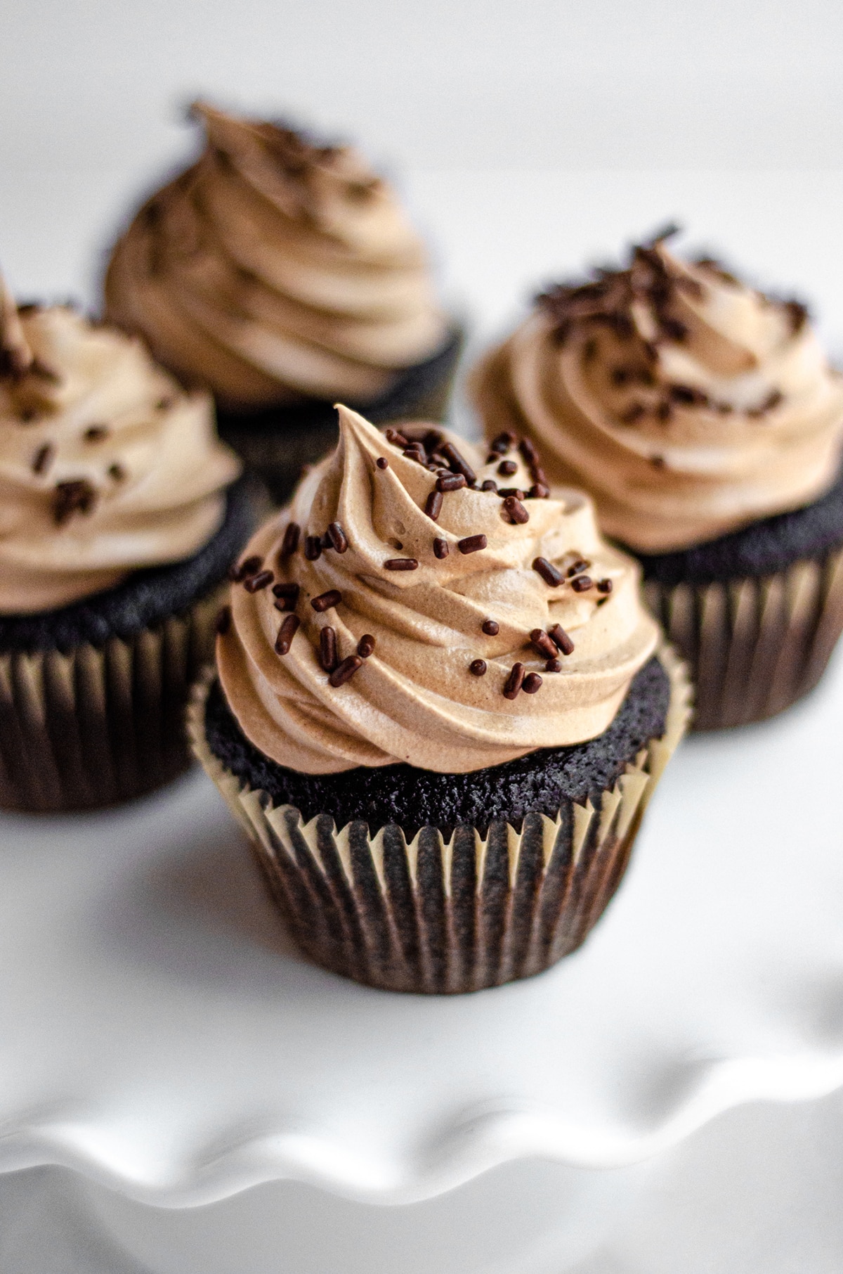 chocolate cupcakes with chocolate swiss meringue buttercream sitting on a white fluted cake stand