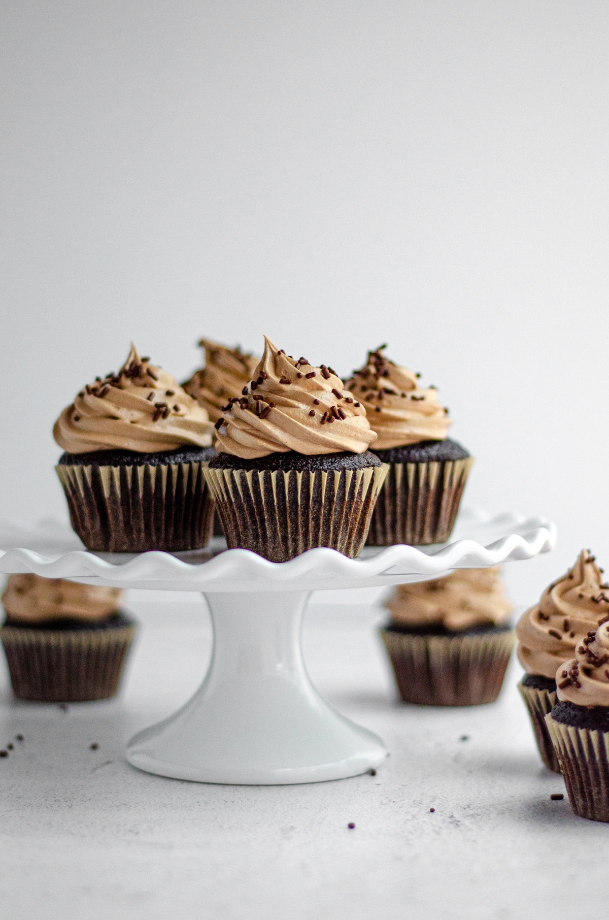 chocolate cupcakes with chocolate swiss meringue buttercream sitting on a white fluted cake stand