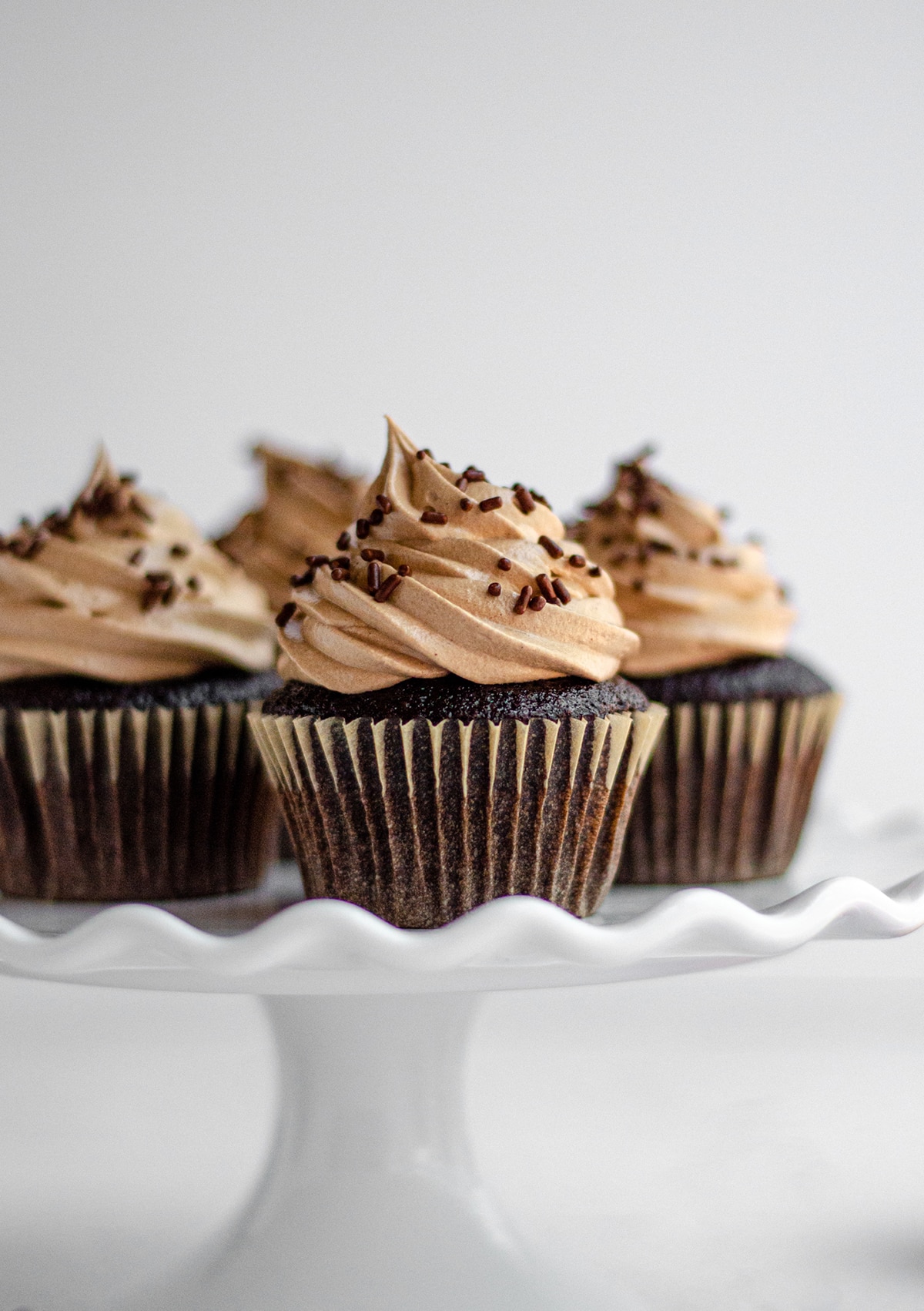 chocolate cupcakes with chocolate swiss meringue buttercream sitting on a white fluted cake stand