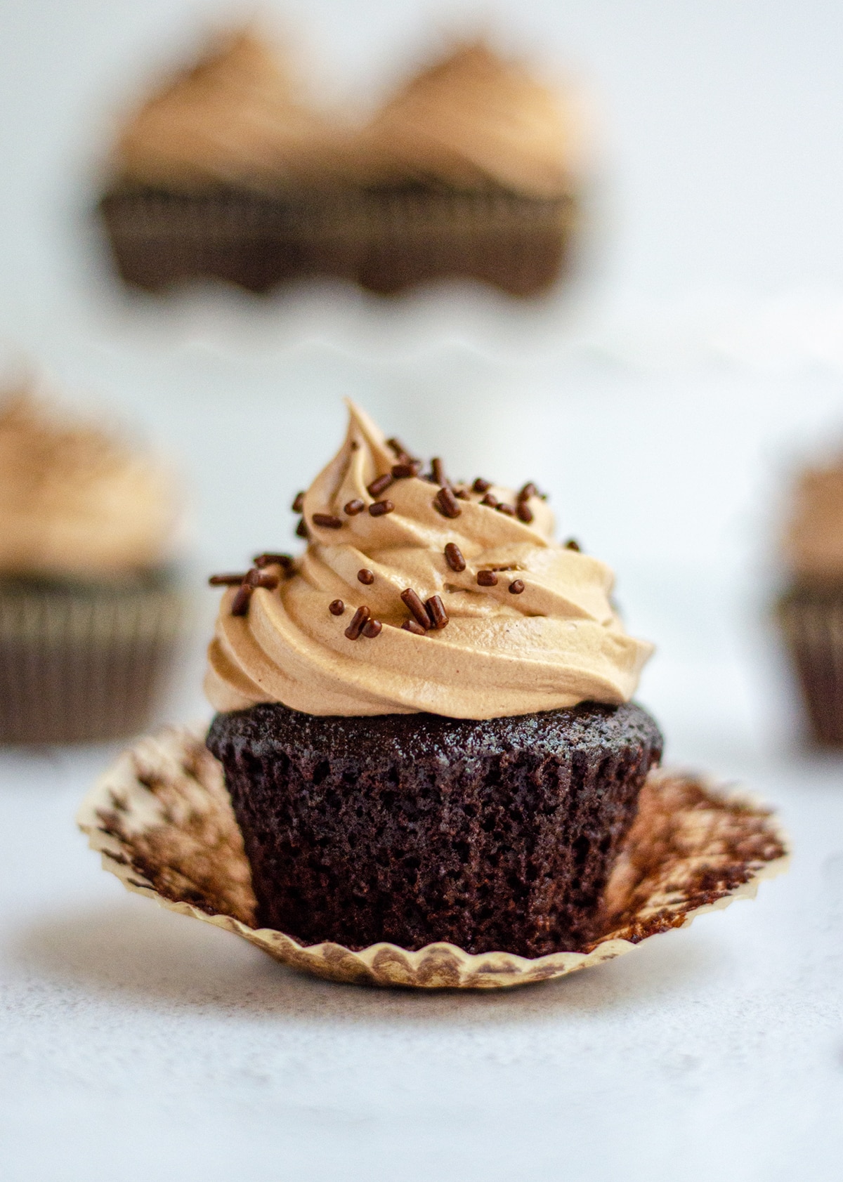 an unwrapped simple chocolate cupcakes with chocolate swiss meringue buttercream and chocolate sprinkles on top