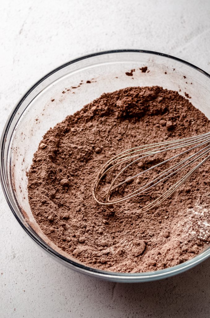 The dry ingredients for chocolate cupcakes in a bowl with a whisk.