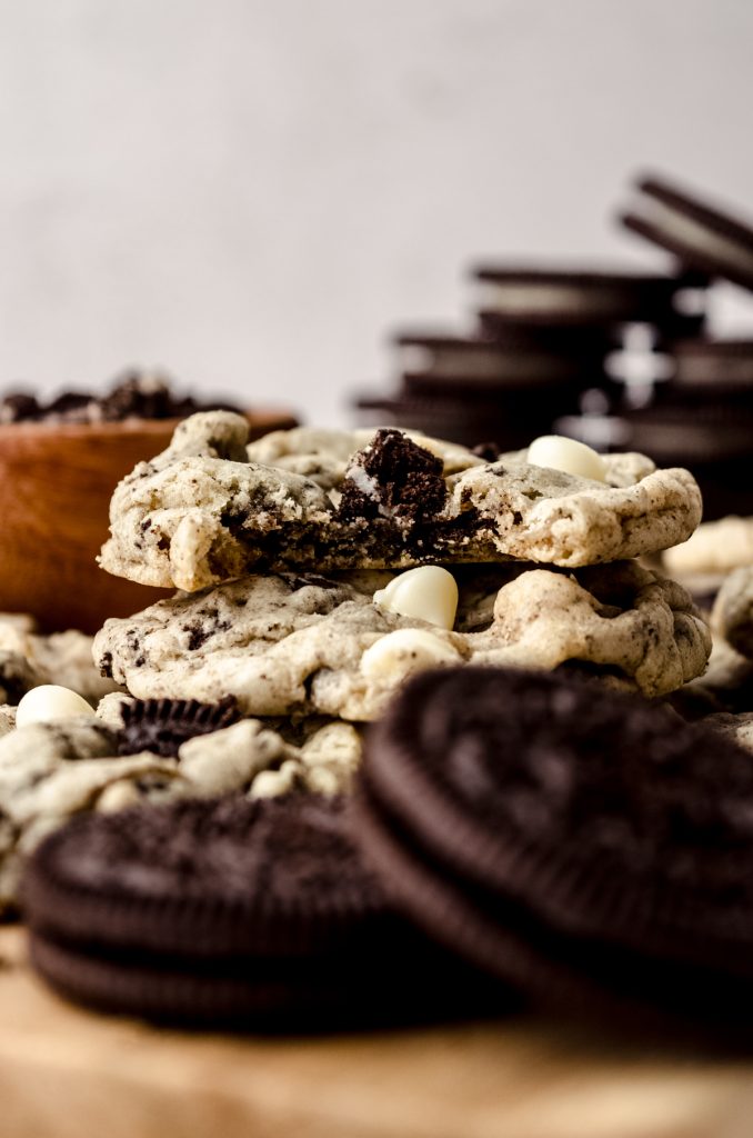 A stack of cookies and cream cookies on a cutting board with Oreo cookies in the foreground and background and a bite has been taken out of the cookie on the top of the stack.