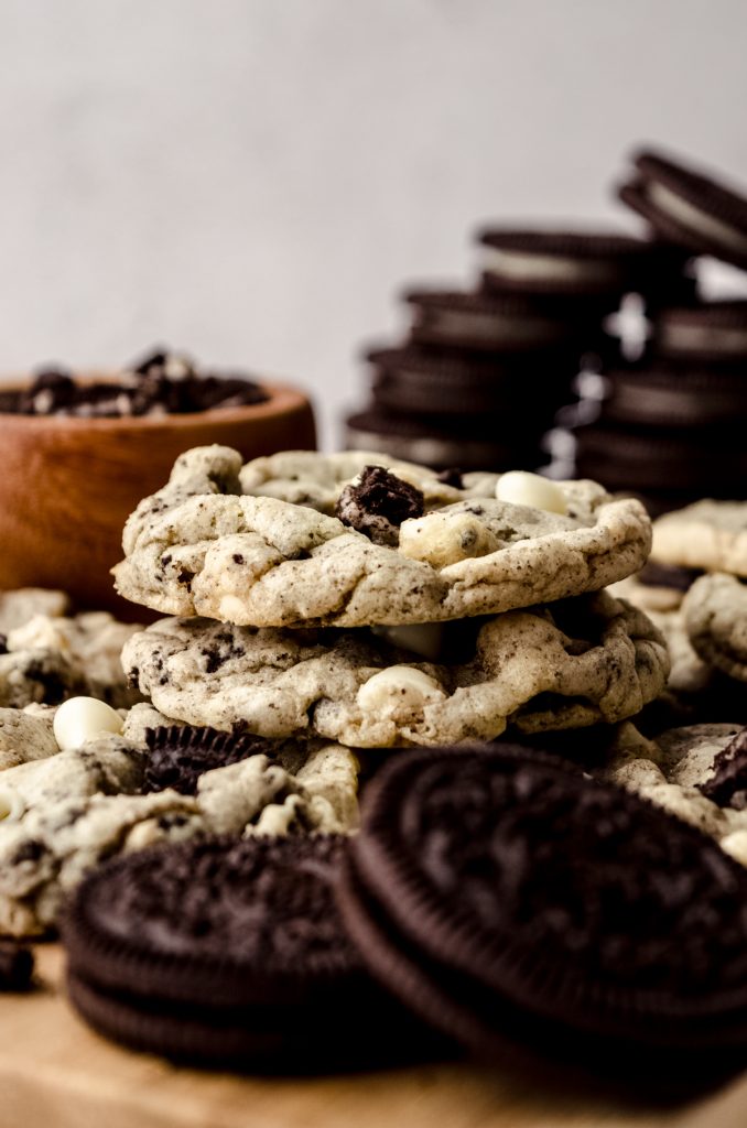 A stack of cookies and cream cookies on a cutting board with Oreo cookies in the foreground and background.