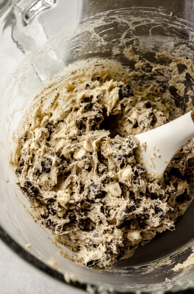 Cookies and cream cookie dough in the bowl of a stand mixer with a spatula in it.