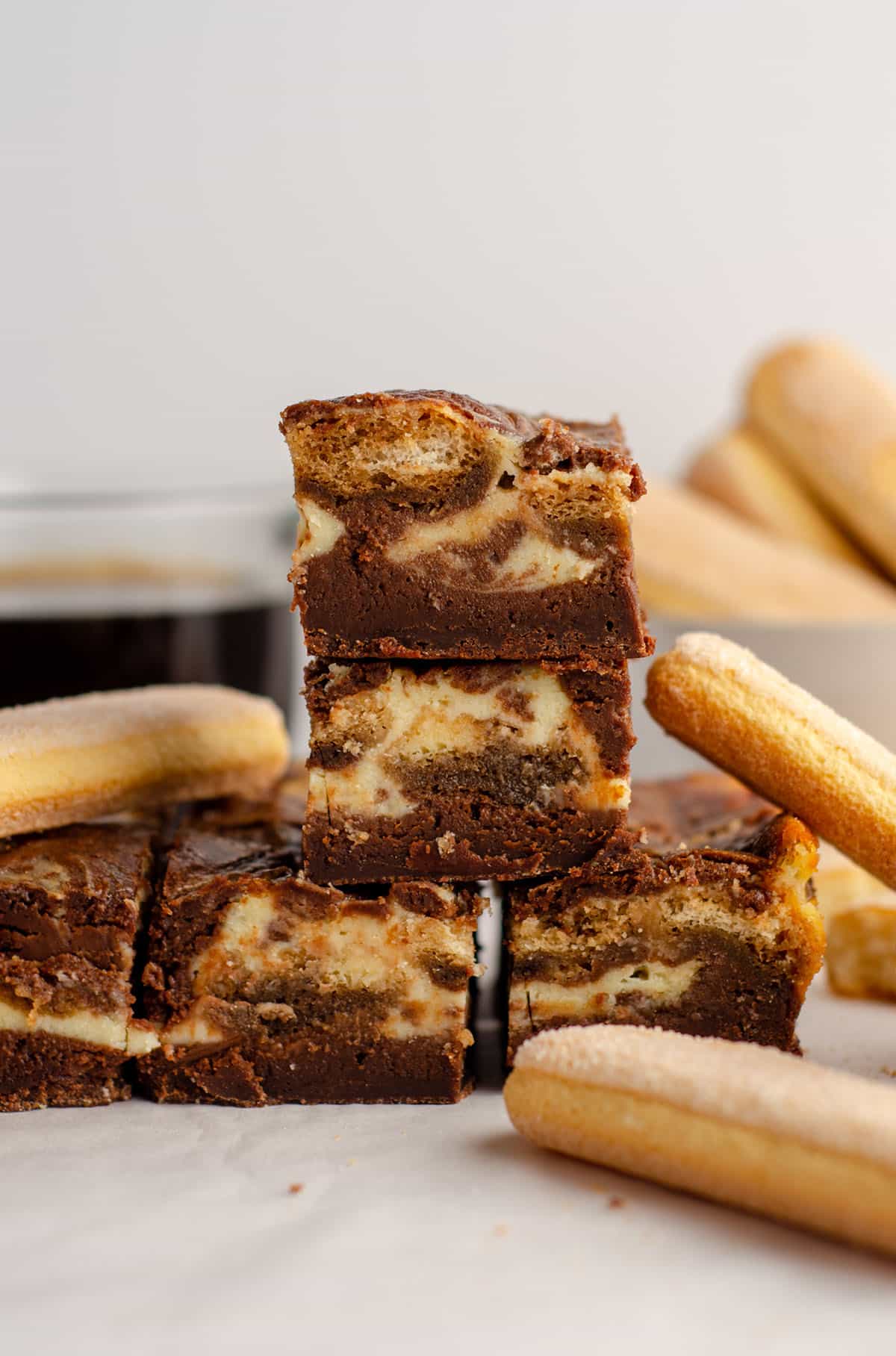 stack of tiramisu brownies with a cup of coffee and ladyfingers in the background